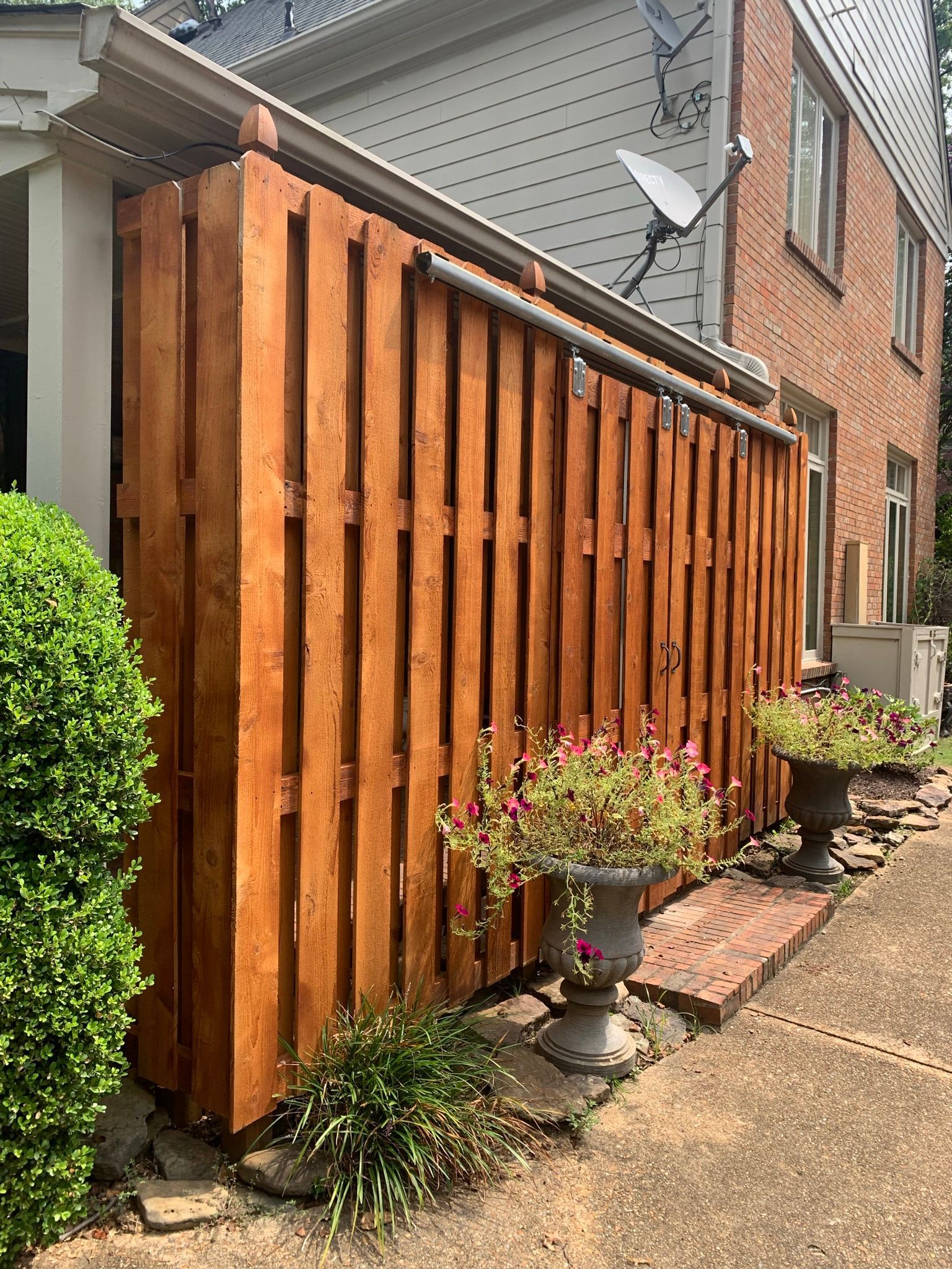 Brown wooden fence with potted flowers in front of a brick building.