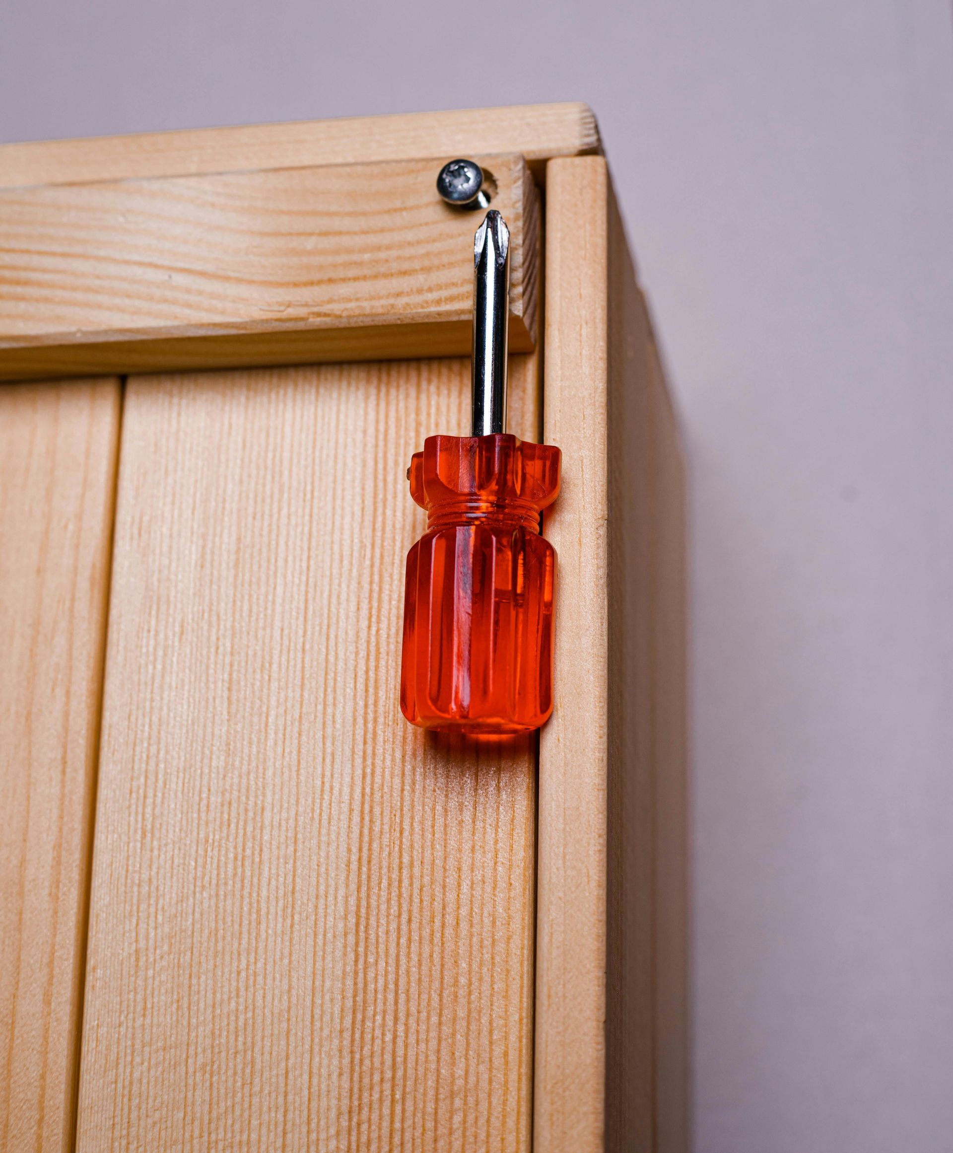 Red screwdriver hanging from a screw on a wooden cabinet.
