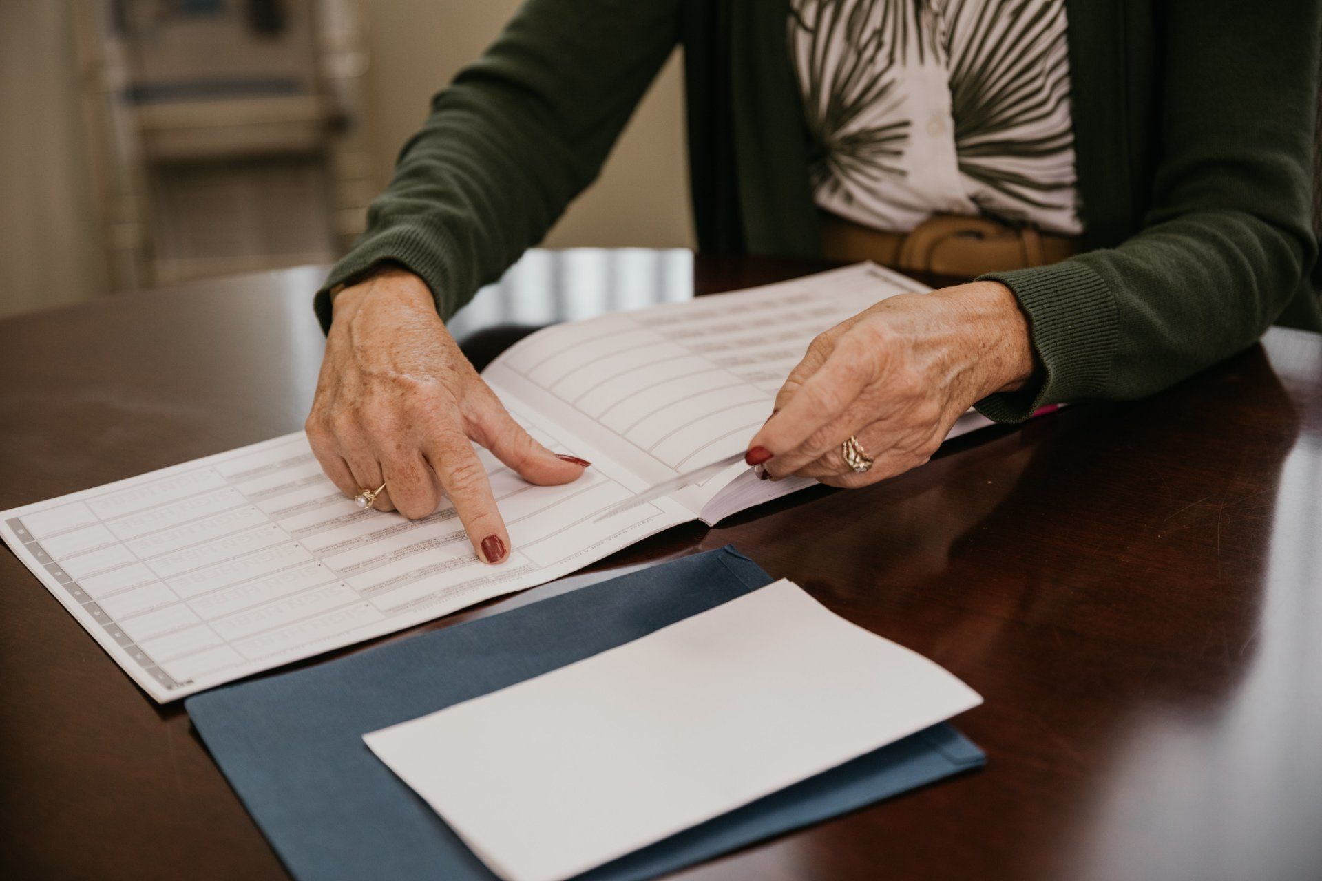 Person pointing at a sheet of paper open on a dark table, with additional paper underneath.