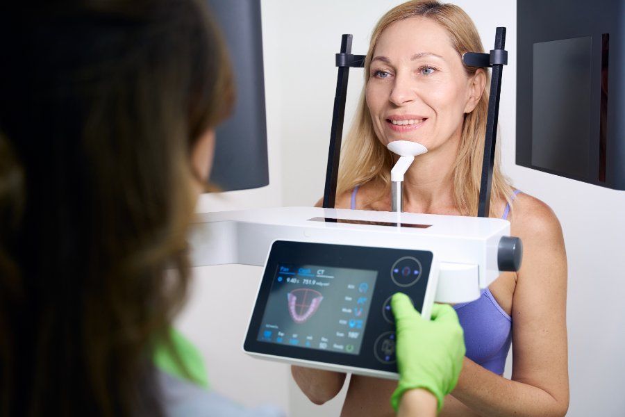 Woman undergoing dental scan. Dentist in green gloves operates the machine, showing scan display.