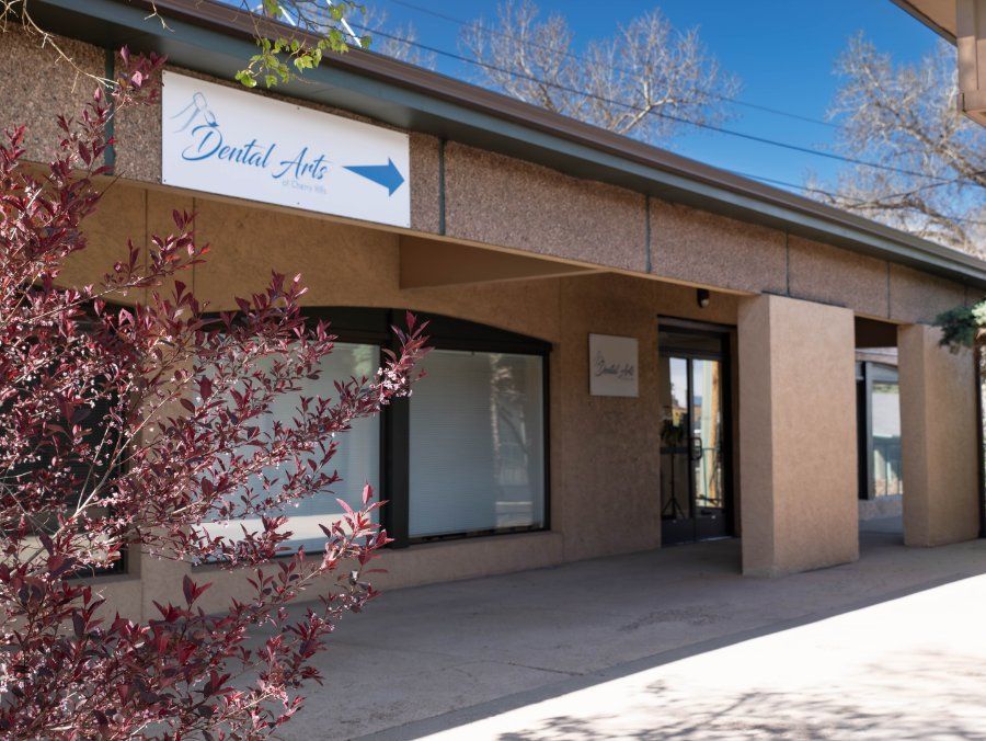 Exterior of Dental Arts office with a sign, arrow, and entrance. Brown and tan building with bushes.