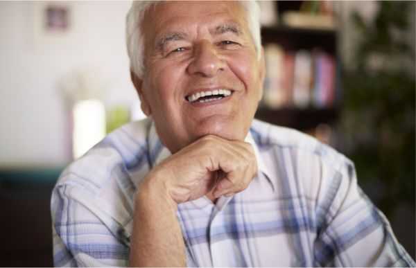 Smiling older person with white hair, hand on chin, wearing a plaid shirt.
