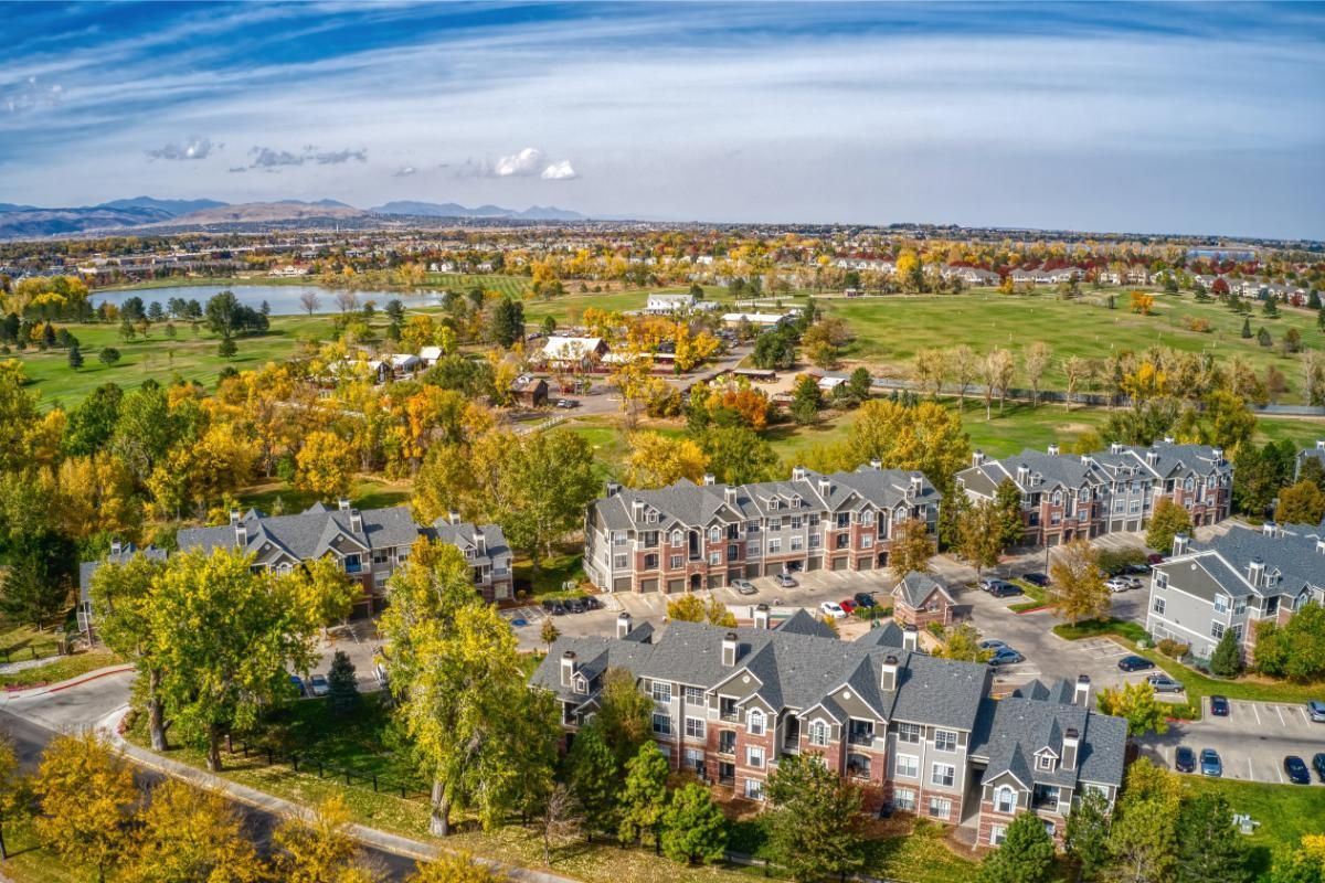 Aerial view of apartment buildings surrounded by fall foliage, a golf course, and mountains.