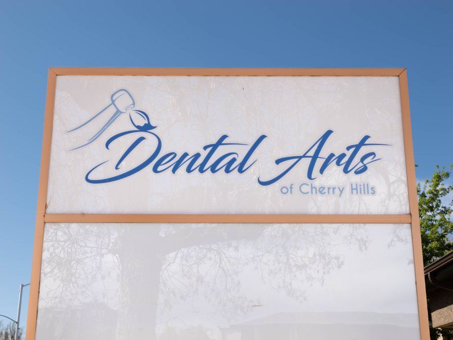 Sign for Dental Arts of Cherry Hills with a blue logo on a white background, against a blue sky.