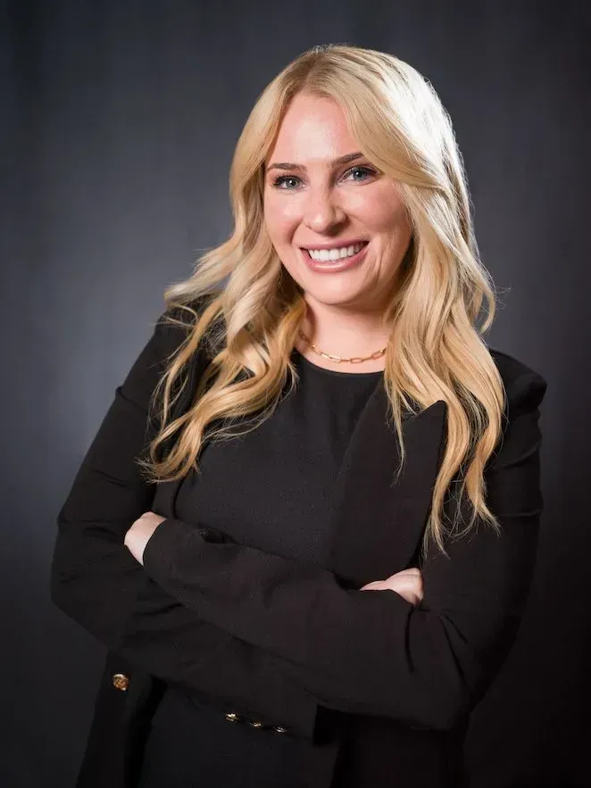 A woman in a black dress is smiling with her arms crossed.