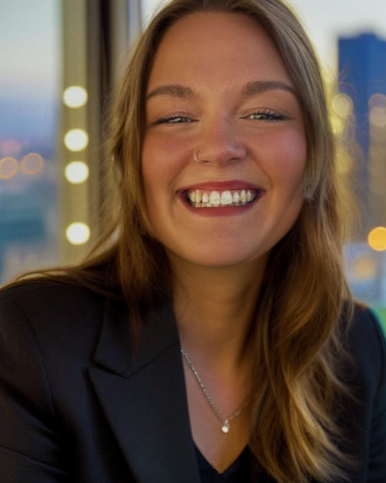 A woman wearing a black jacket and a necklace is smiling