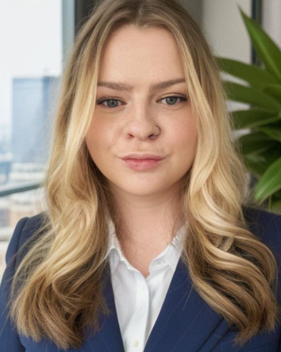 A woman in a blue jacket and white shirt is standing in front of a window.