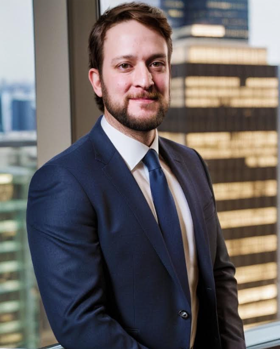 A man in a suit and tie is standing in front of a window