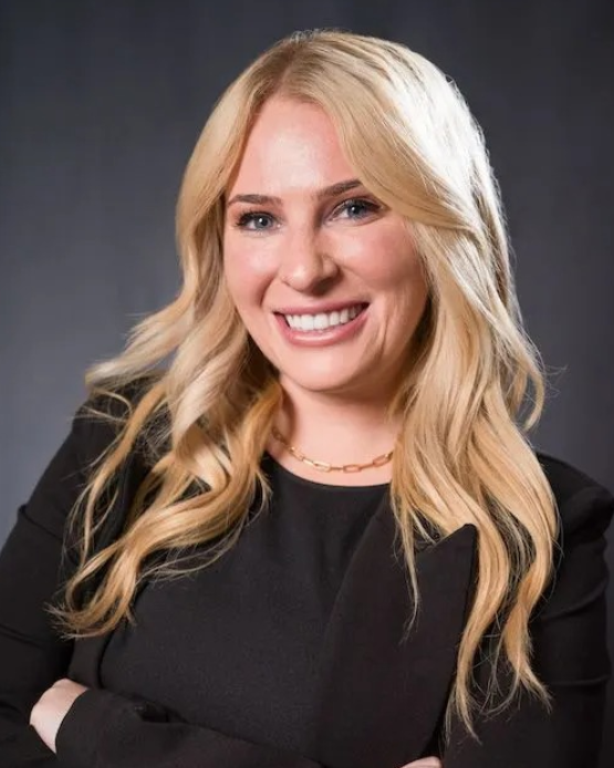 A woman in a black dress is smiling with her arms crossed.