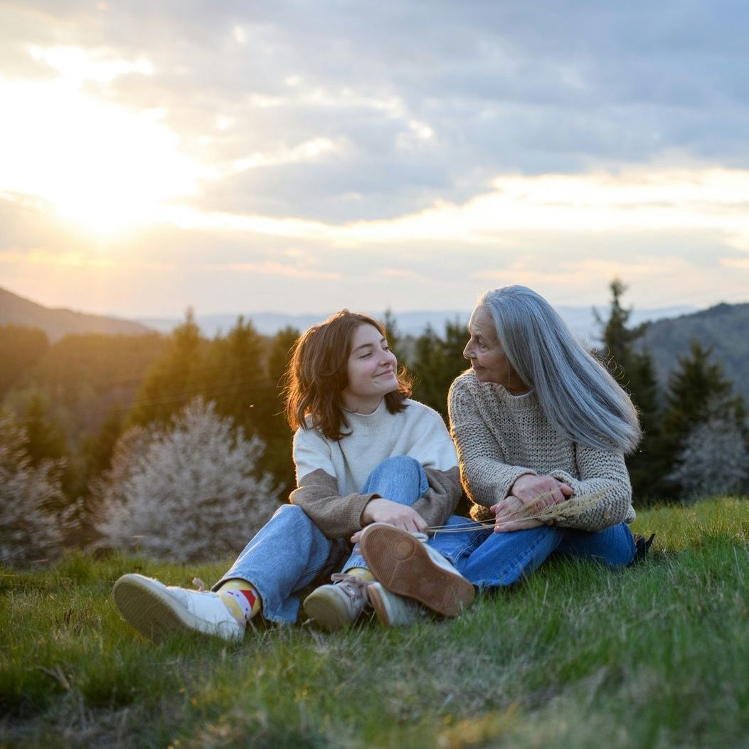Two women are sitting on top of a grass covered hill.