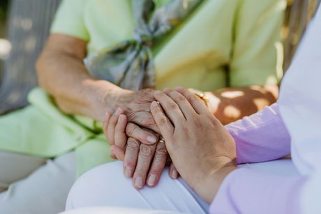 A nurse is holding the hands of an elderly woman.