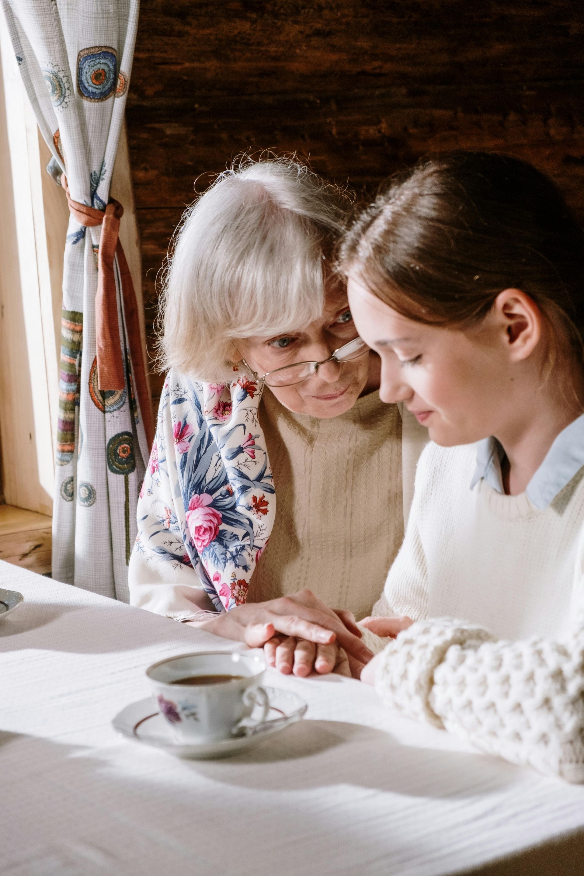 An elderly woman and a young girl are sitting at a table holding hands.