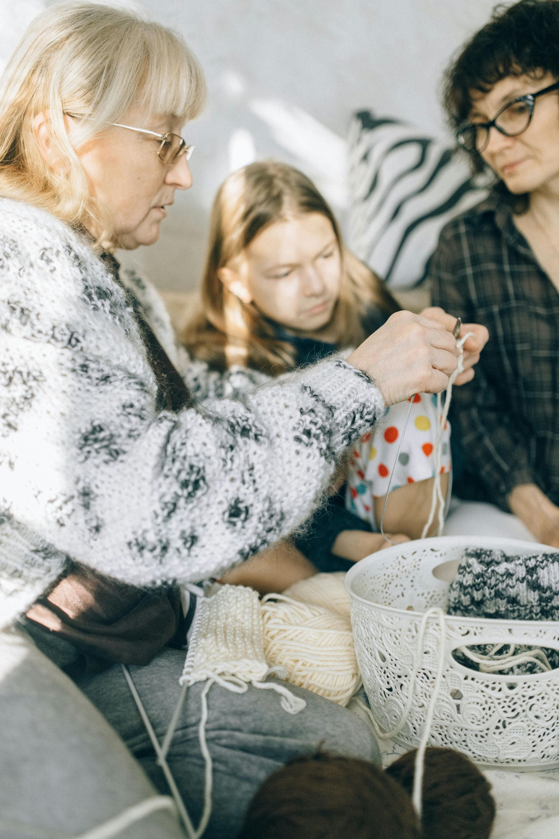 A group of people are sitting on a couch knitting together.