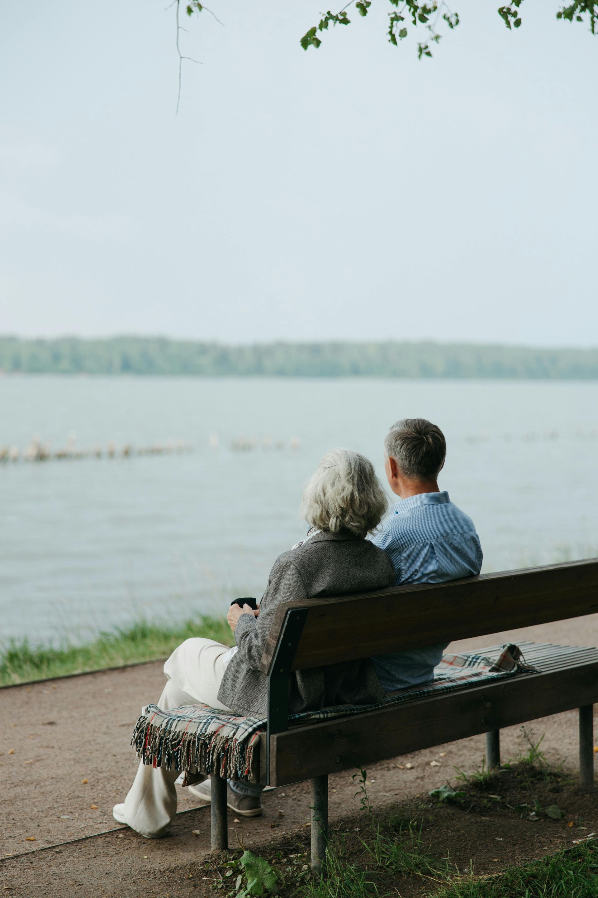 An elderly couple is sitting on a bench looking at the water.