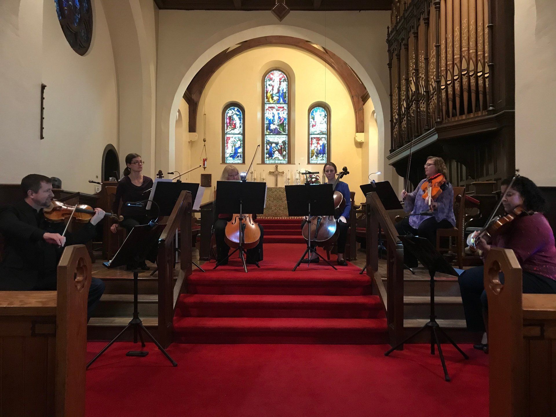 String quartet performing on a church stage with stained glass and red carpet.