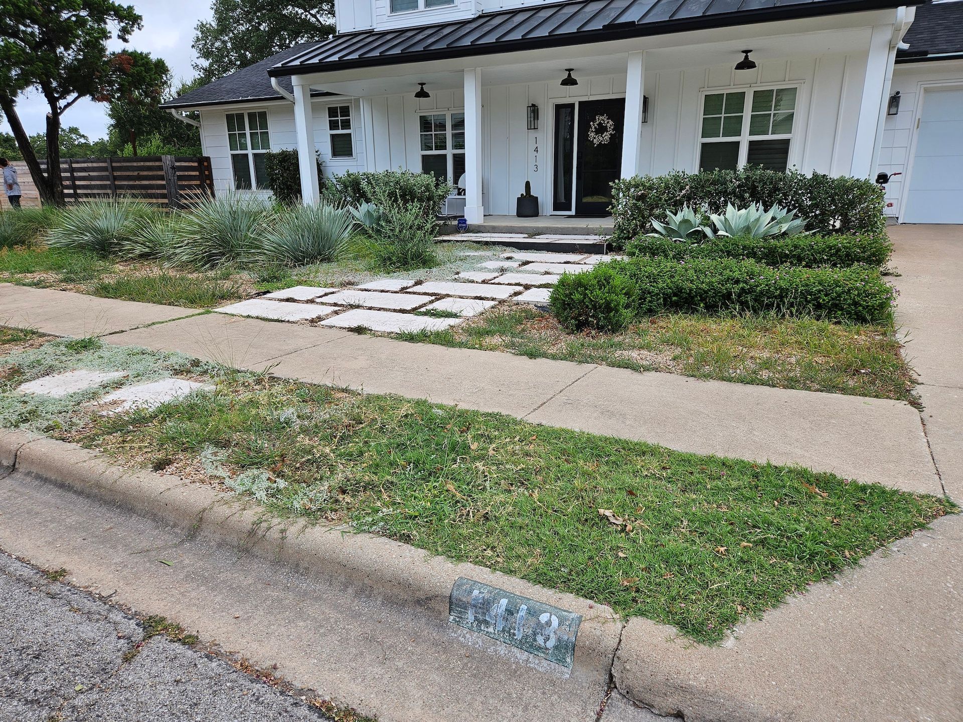 A white house with a black roof and a stone walkway in front of it.
