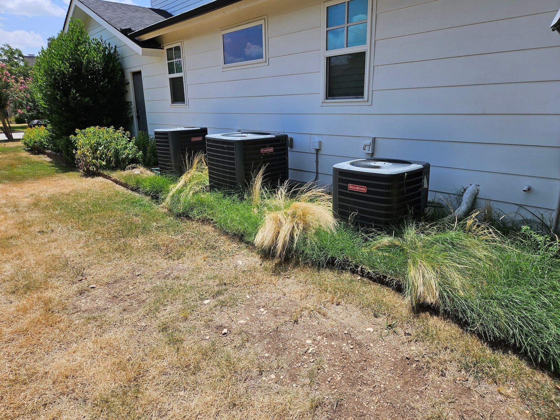A row of air conditioners are sitting on the side of a house.