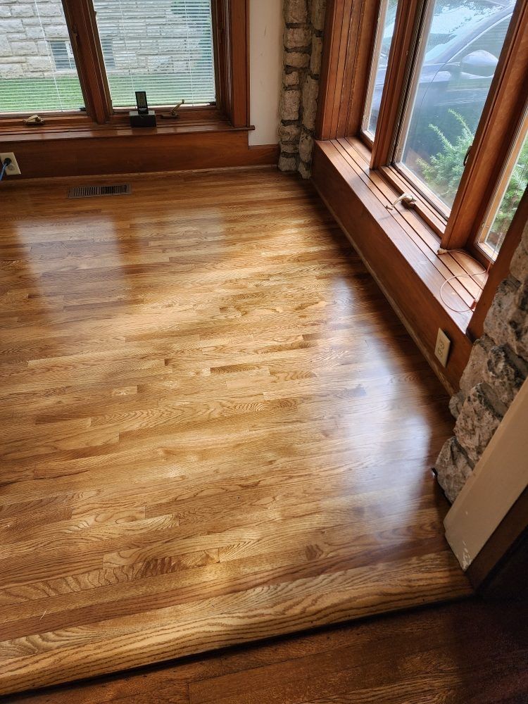 Hardwood floor in a room with large windows and wooden trim.