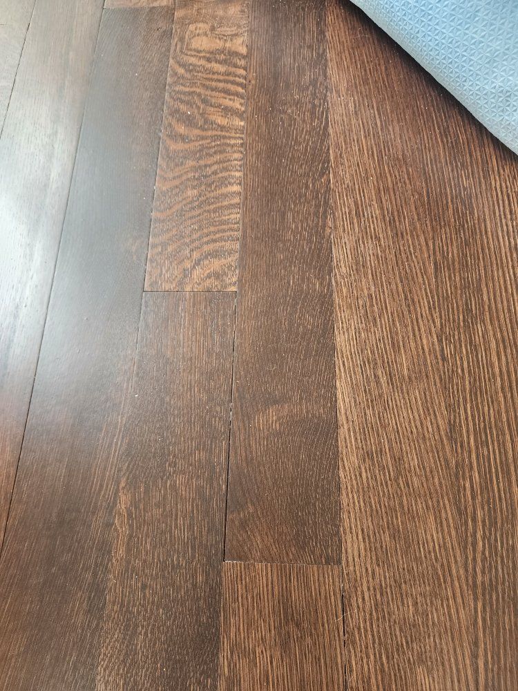 Close-up of dark brown wooden floorboards with a section of blue fabric at the edge.