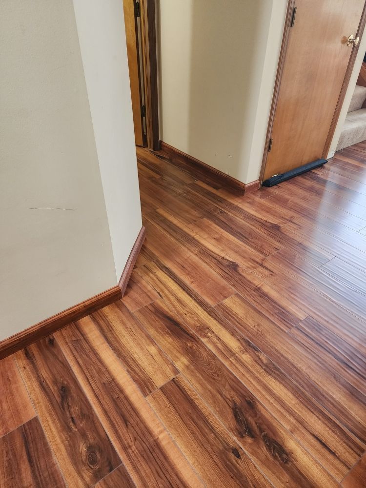 Hardwood floors in a hallway with brown trim and beige walls, leading to a door.