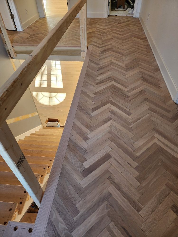 Herringbone wood floors beside a staircase with a wooden handrail and a window below.