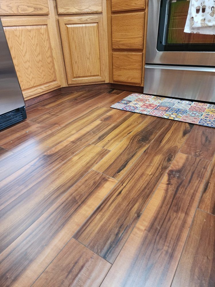 Wooden kitchen floor with brown planks, near cabinets and a stove.