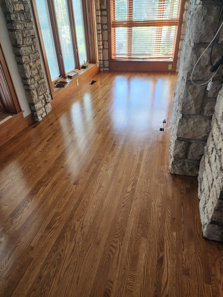 Wooden floor, bright oak color, reflecting light from a window, next to stone wall, and window frame.