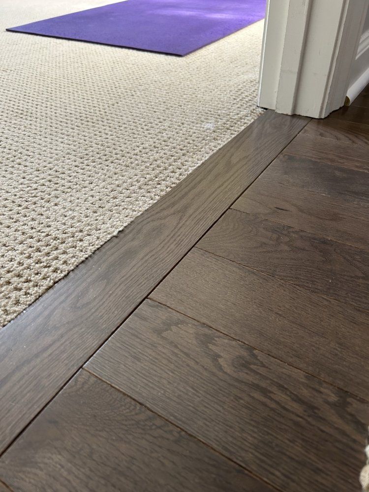 Transition between dark wood flooring, a beige carpet, and a purple yoga mat visible through a doorway.