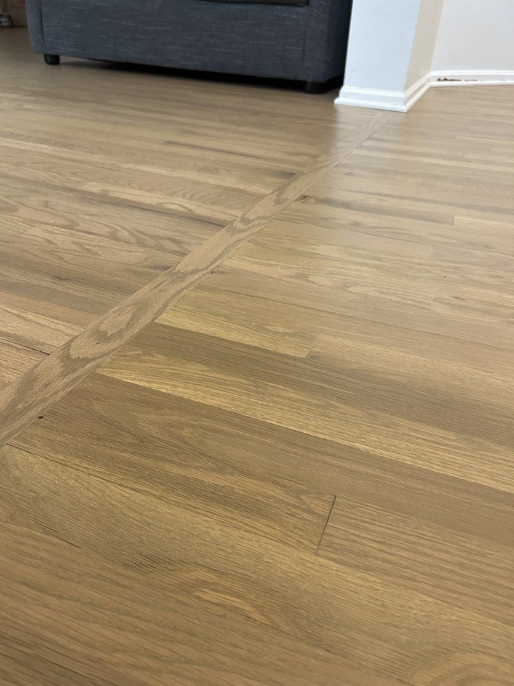 Wood flooring with a cross-shaped pattern and a neutral color, reflecting light.