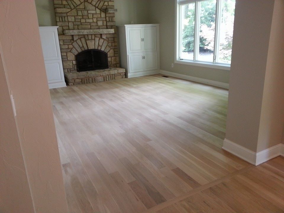 Living room with light wood floors, a stone fireplace, white cabinets, and a window.