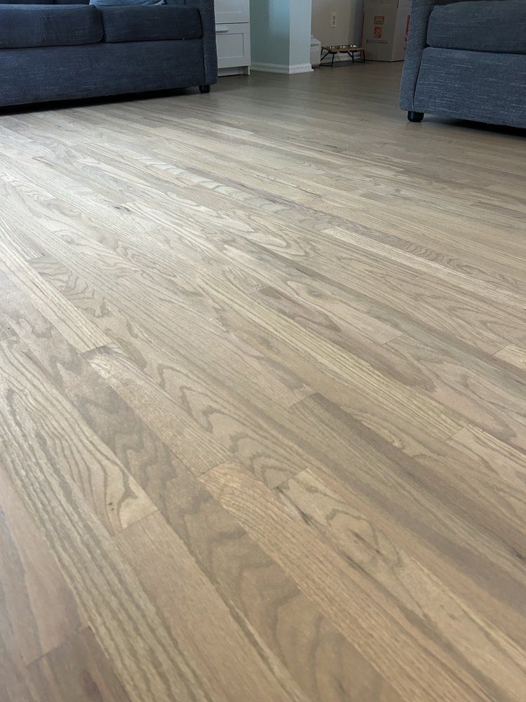 Light-colored wood floor with visible grain detail, partially visible blue couches.