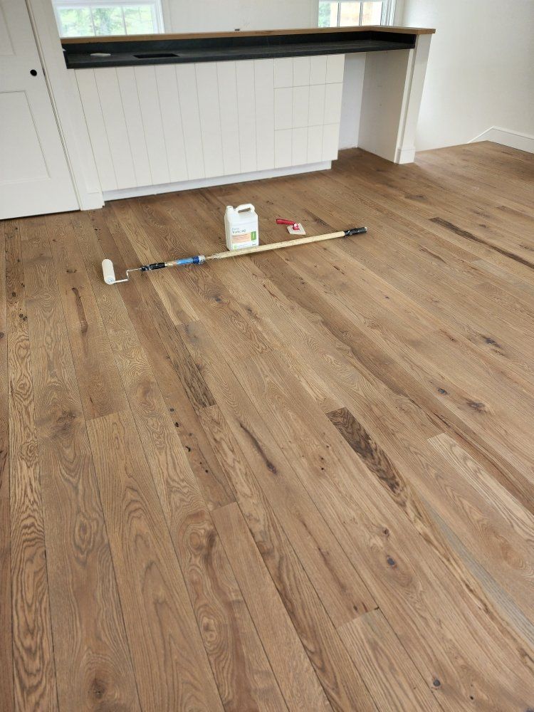 Hardwood floor being refinished with a paint roller and a container of finish.