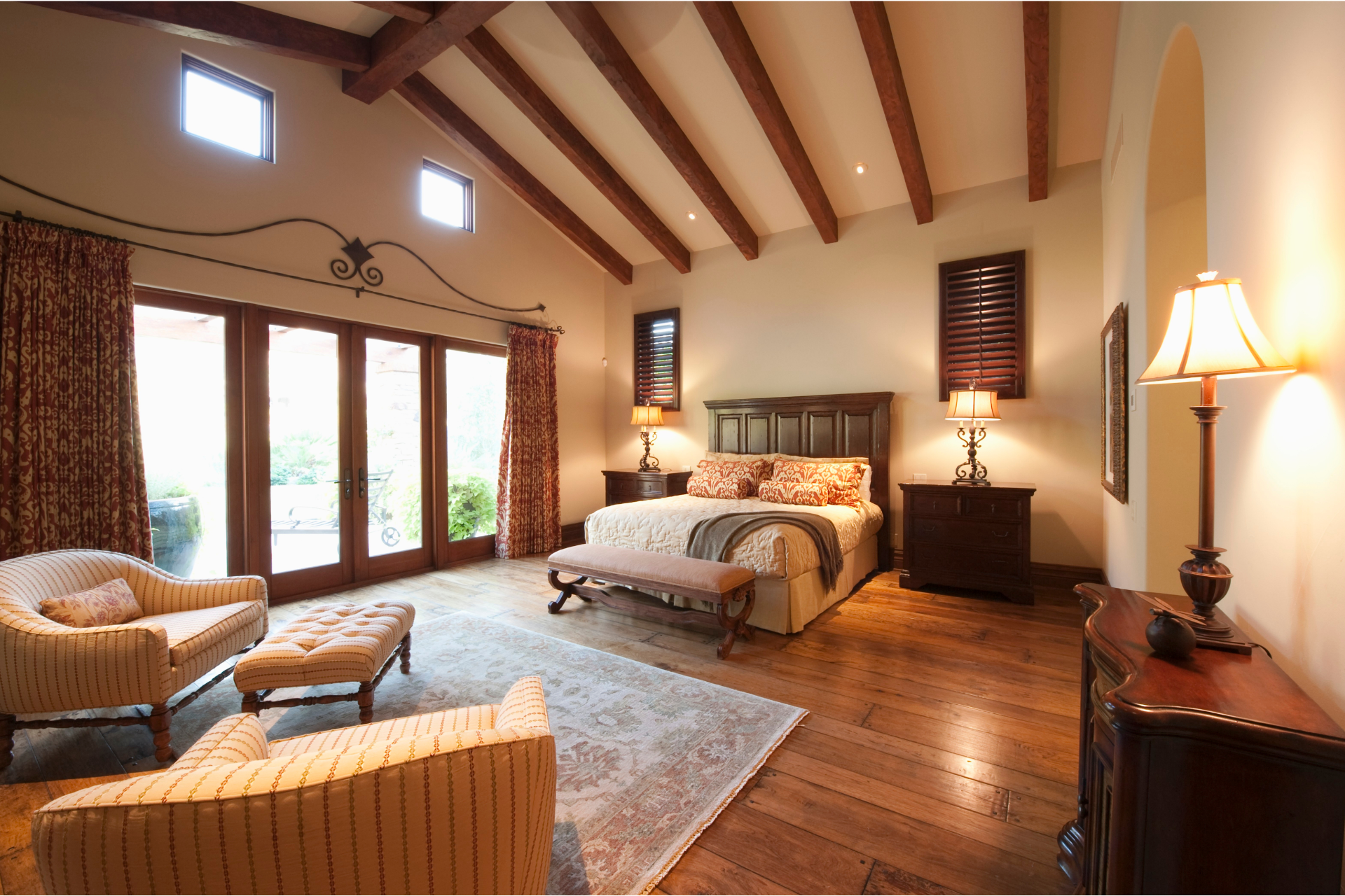 Bedroom with dark wood beams, bed, seating area, and French doors.