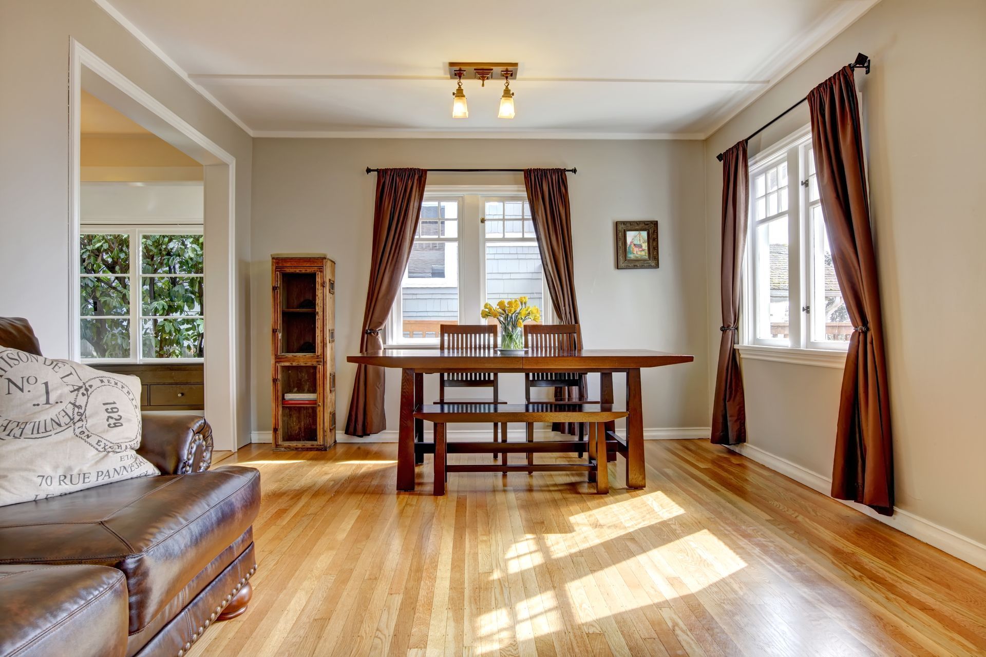 Dining room with wooden table, chairs, hardwood floors, and brown curtains.
