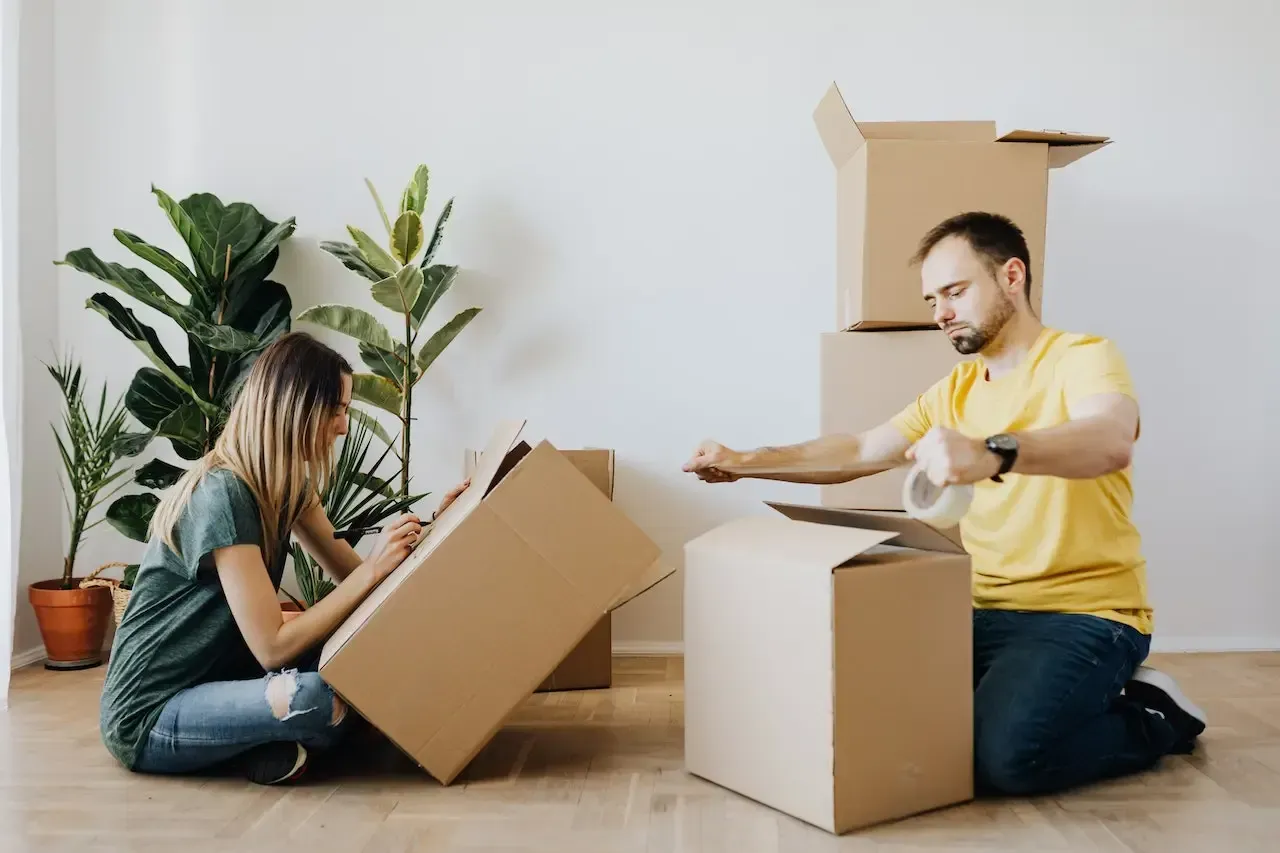 A man and a woman are sitting on the floor packing boxes.