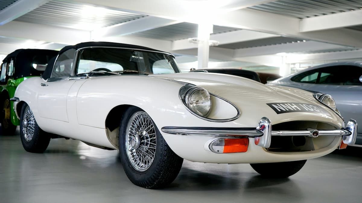 A white car is parked in a garage next to other cars.