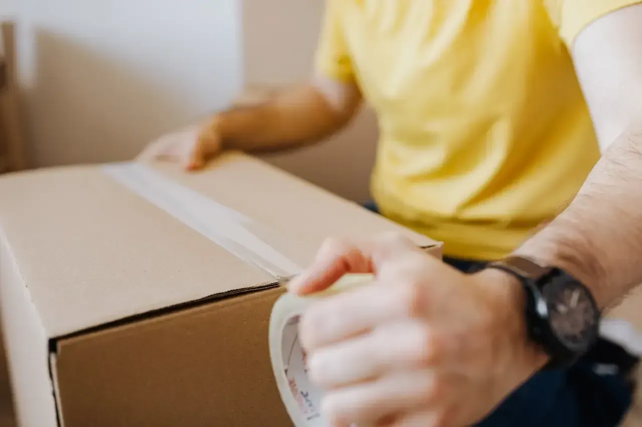 A man is packing a cardboard box with tape.