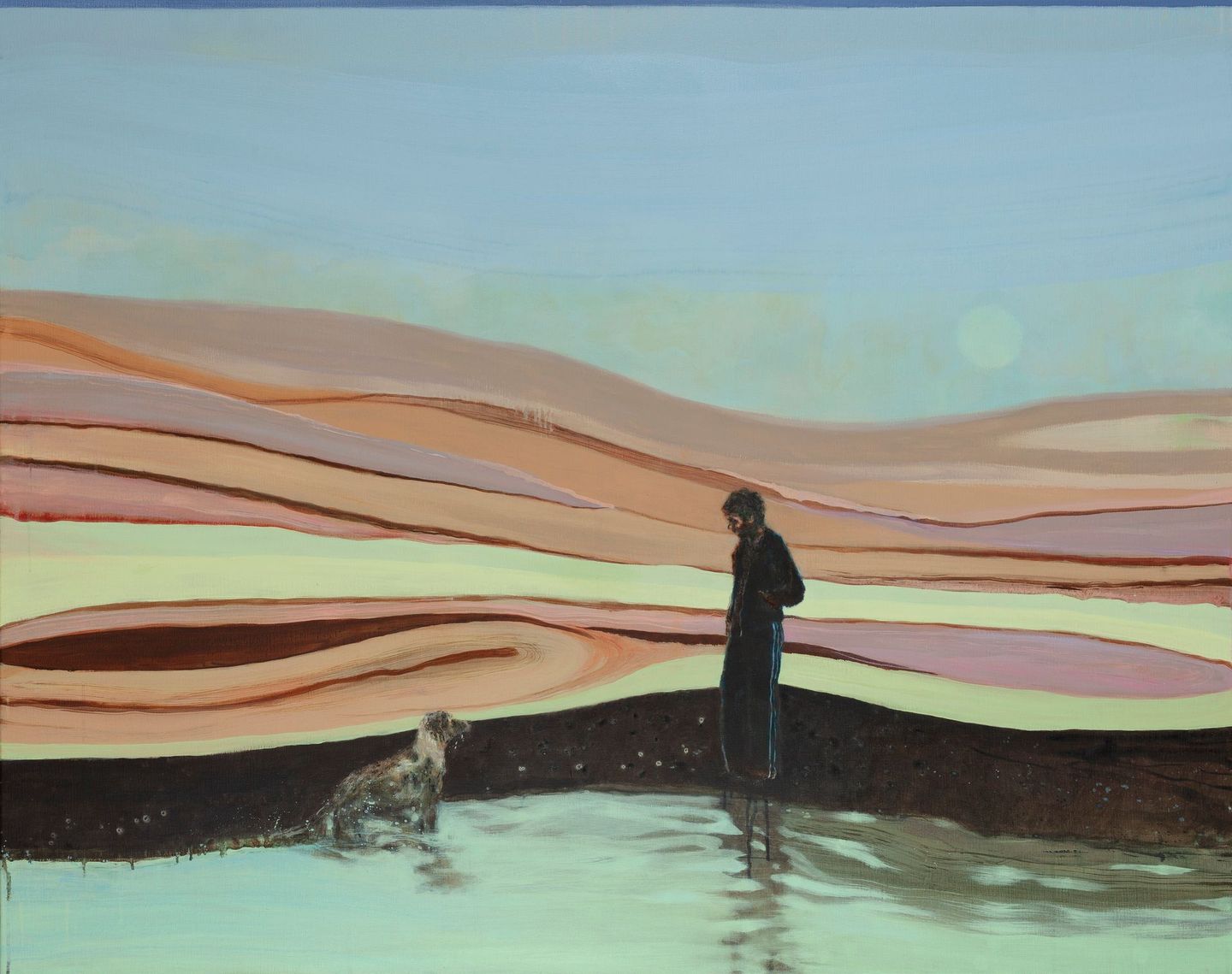 Een persoon in zwart staat naast een hond in ondiep water, met op de achtergrond pastelkleurige heuvels onder een blauwe hemel.