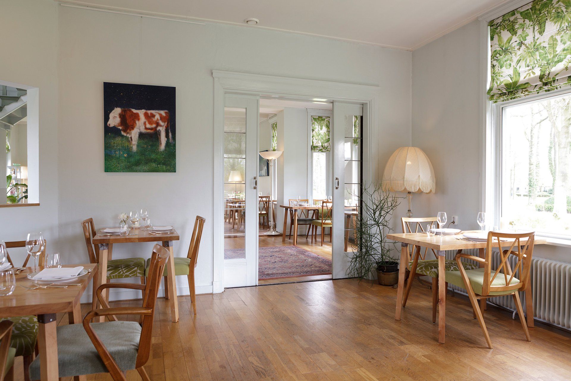 Interieur van het restaurant: gedekte tafels, schilderij van een stier op de muur, open deur naar een ander eetgedeelte.