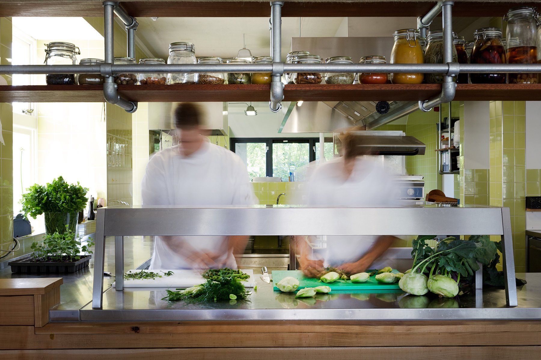 Chefs bereiden eten in een professionele keuken, groenten op een metalen aanrecht, vage bewegingen.