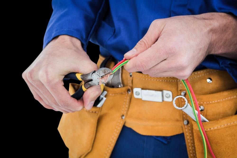 Electrician stripping wire with pliers, wearing blue shirt and tool belt.