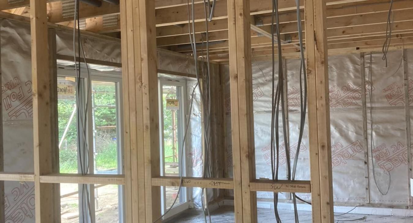 Wooden frame of a building under construction, with windows and electrical wiring visible.