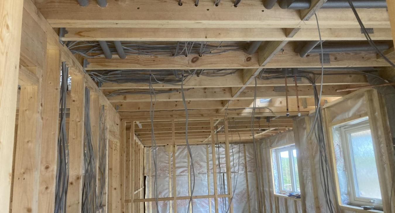 Interior view of a building under construction, showing wooden framing, exposed wires, and plumbing in the ceiling.