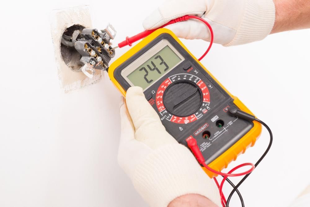 Person in gloves using a multimeter to test an electrical outlet, displaying a reading of 24.3.