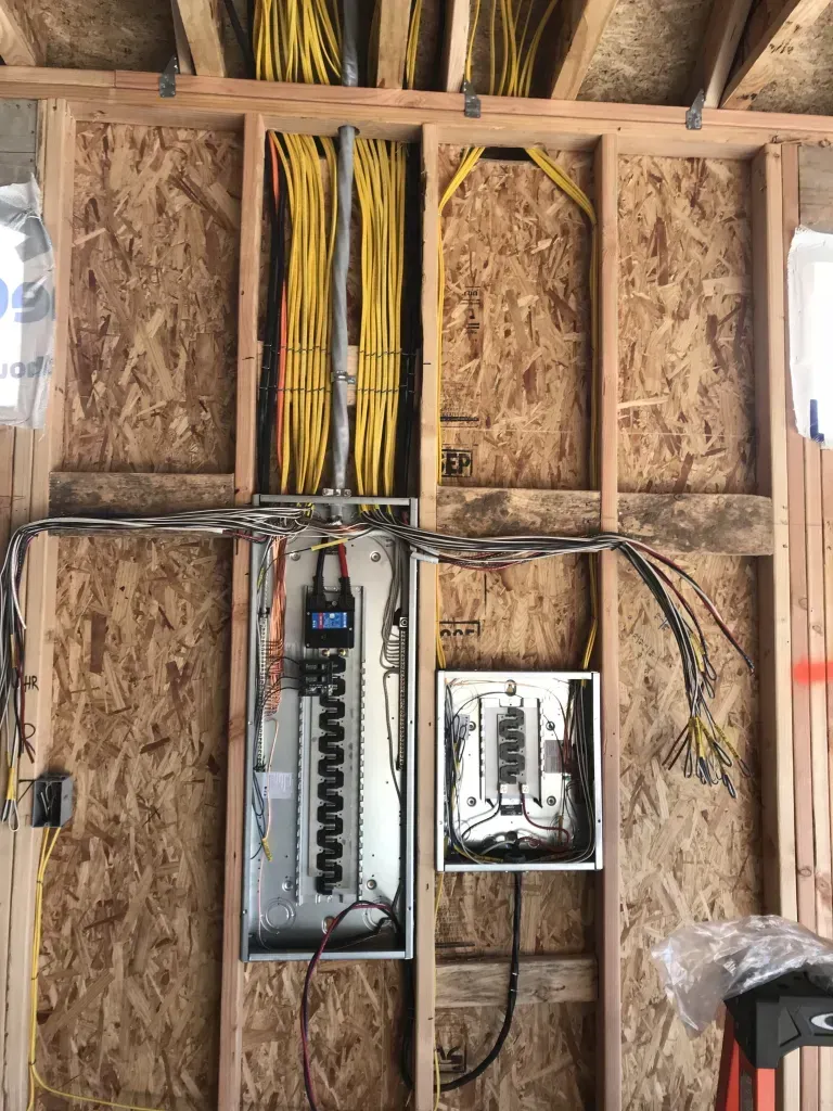 Electrical panel installation in a wood-framed wall. Yellow and black wires are visible.