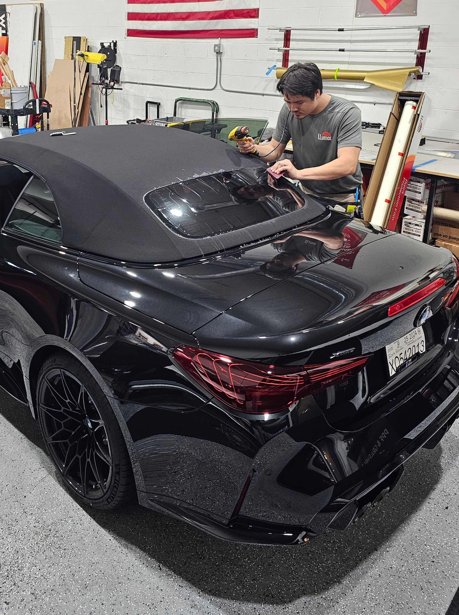 A man is working on a black convertible car in a garage.