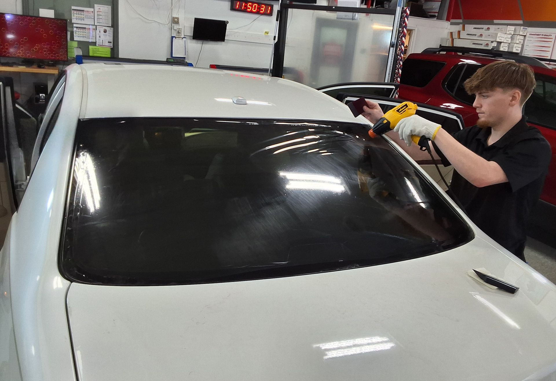 A man is applying window tinting to a white car.
