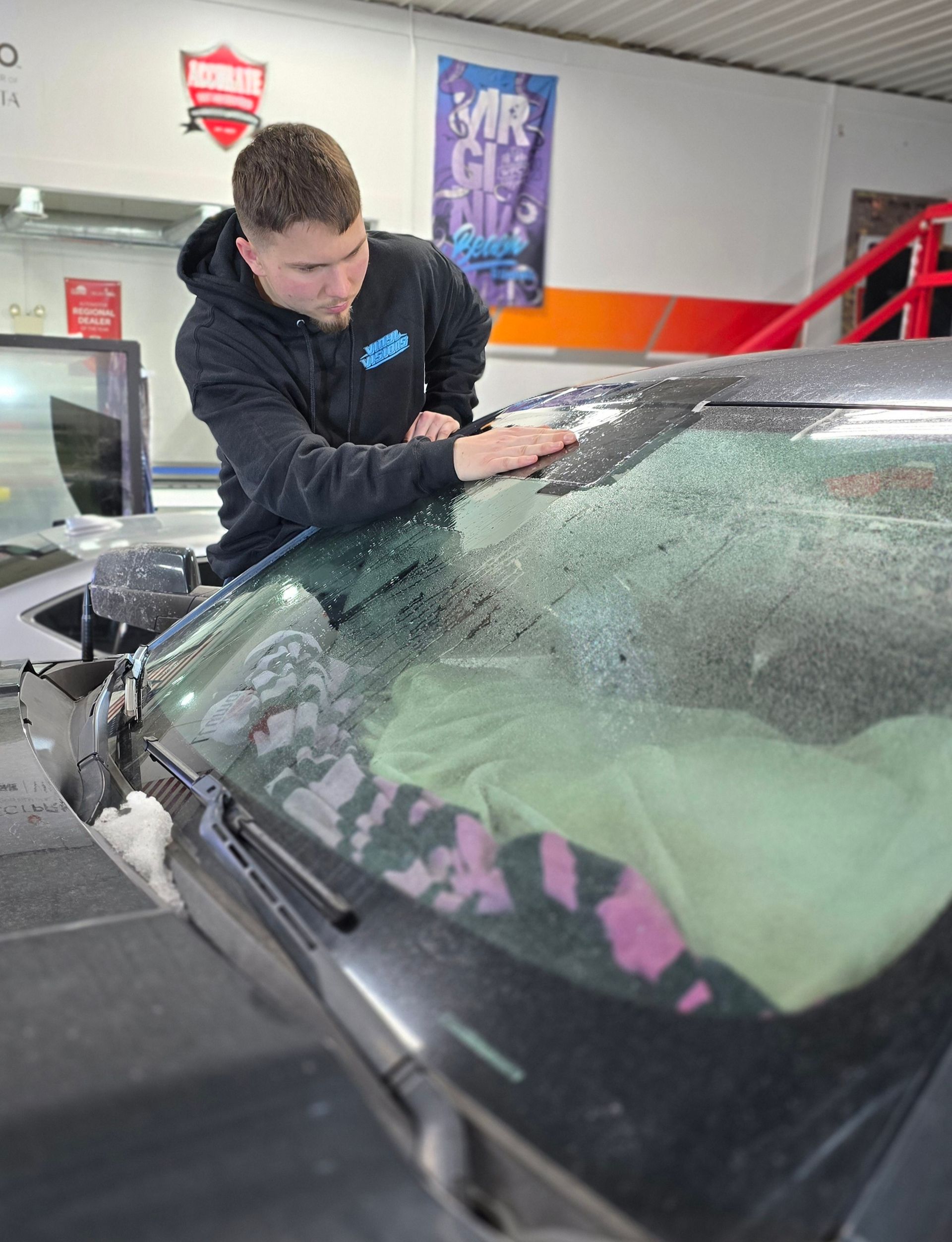 A man is working on a car windshield in a garage.