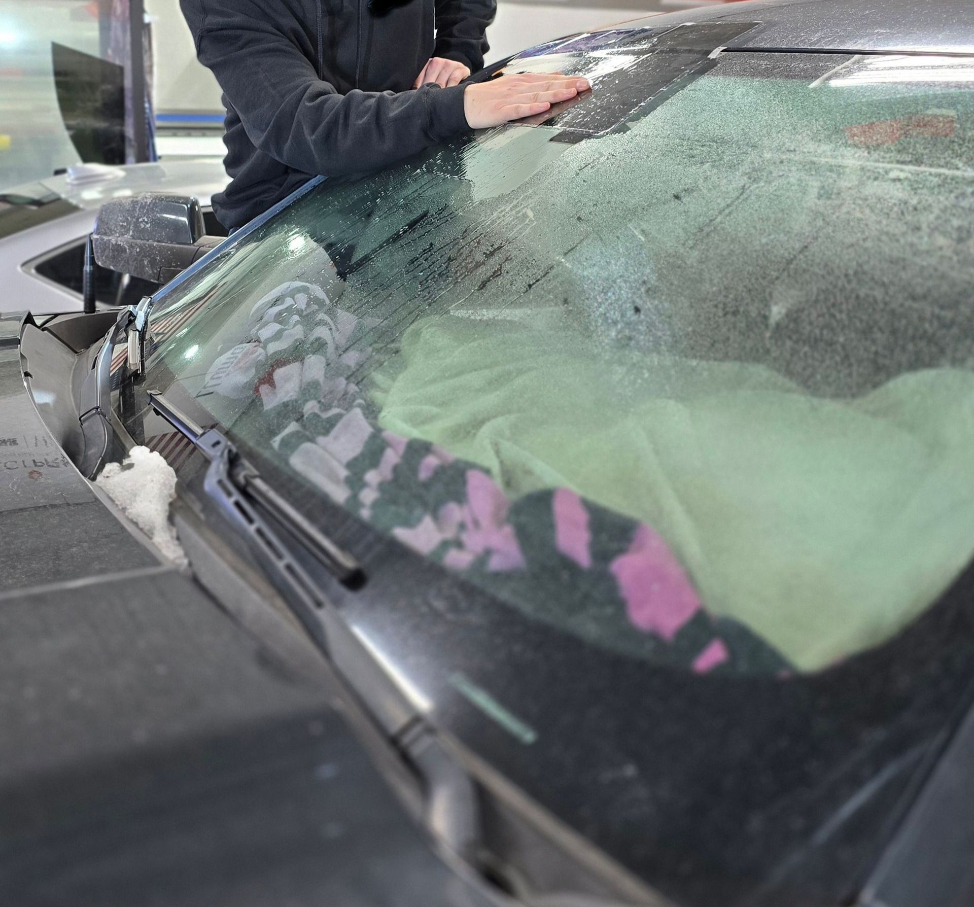 A man is working on a car windshield in a garage.