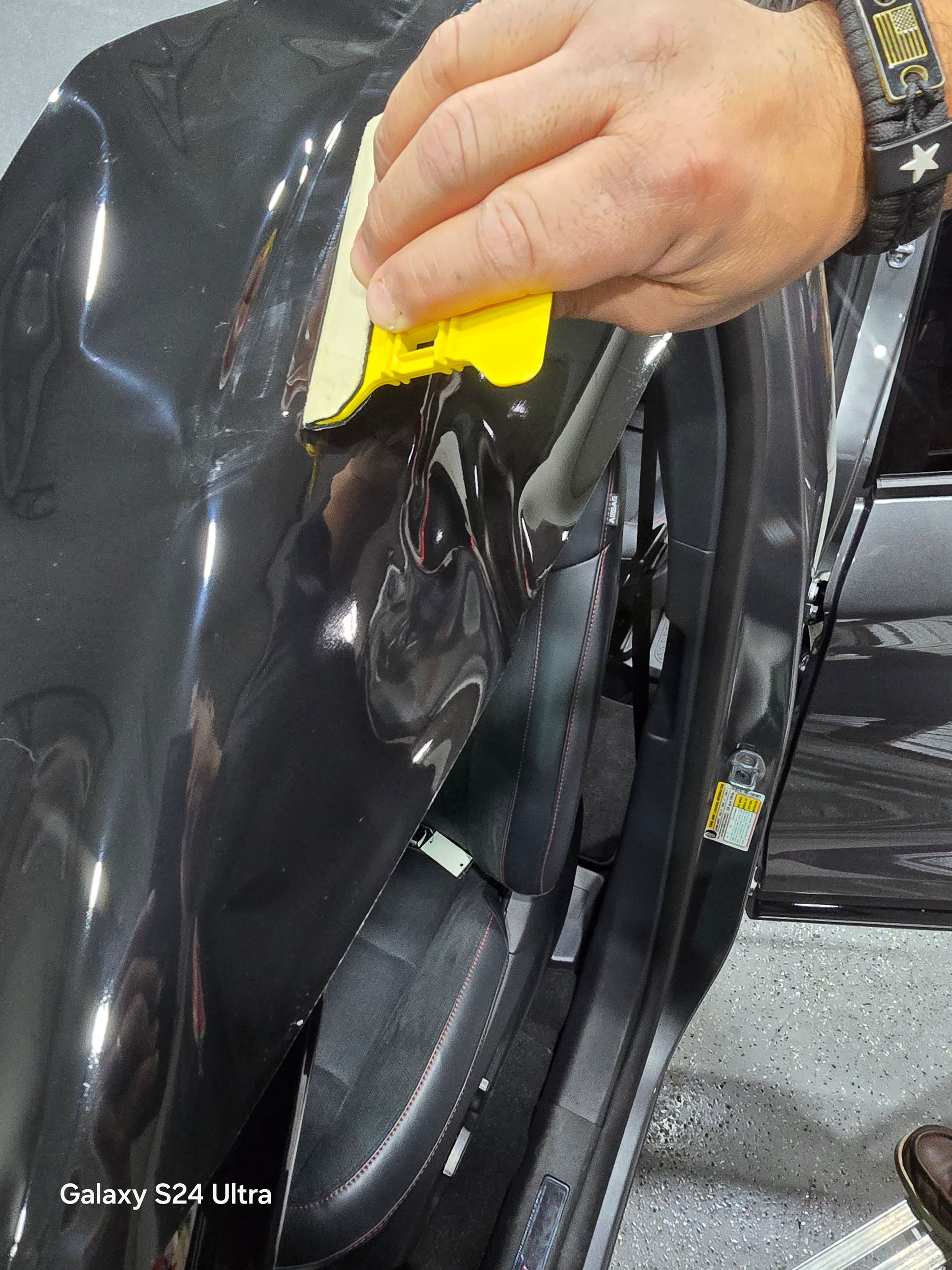 A person is cleaning a car with a yellow sponge.